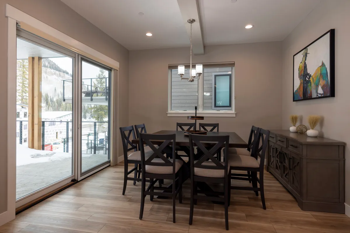A stylish dining area featuring a spacious table beneath a striking chandelier, flanked by large windows that bring the outdoors inside. The arrangement is perfect for shared meals, celebrations, and enjoying the breathtaking scenery.