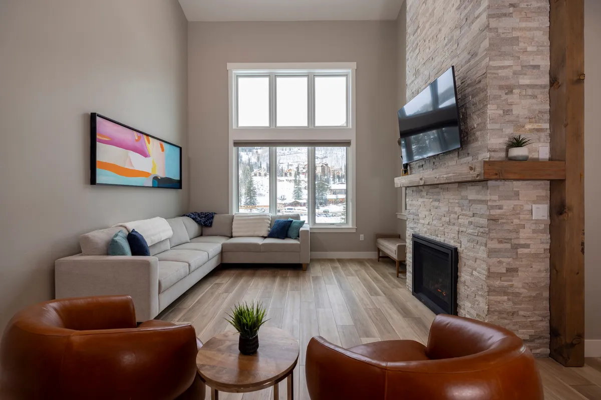 A warm, inviting great room with a cozy sectional sofa, stone fireplace, and large windows that frame sweeping mountain views. The space is bathed in natural light, and tasteful art provides a modern touch, creating a perfect spot for relaxation and gathering.