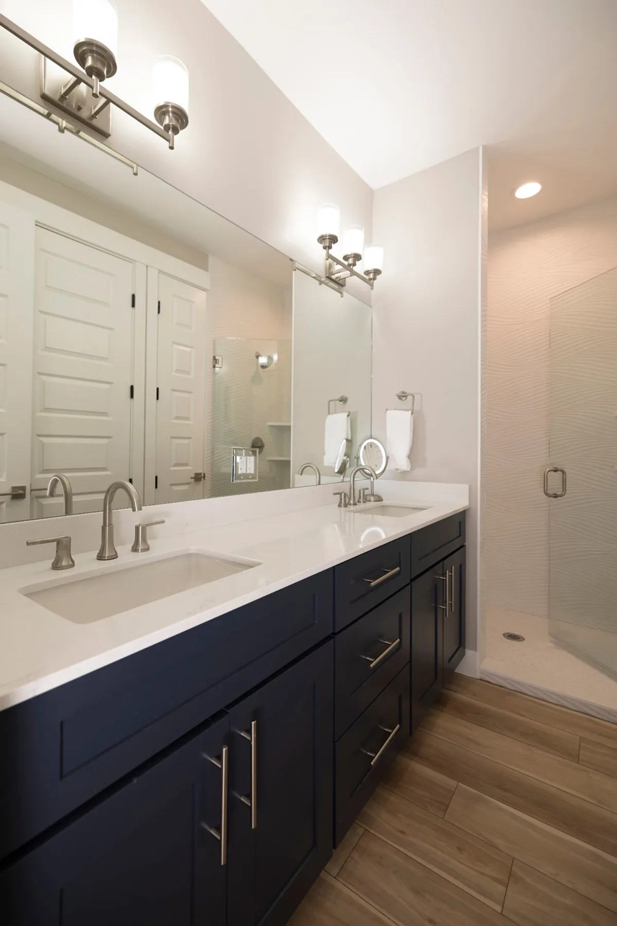 A sophisticated bathroom with a large mirror, double sink vanity, and a spacious glass shower enclosure. The clean lines and calming tones evoke a sense of serenity and private comfort.