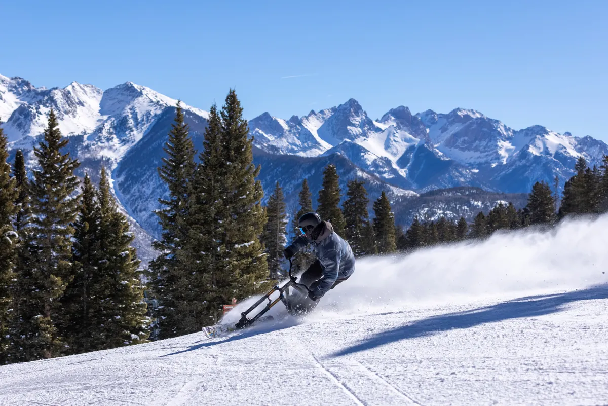 A dramatic exterior scene featuring a skier descending snow-covered slopes, flanked by majestic pine trees and expansive mountain views. The atmosphere is exhilarating and highlights the proximity to thrilling outdoor activities.