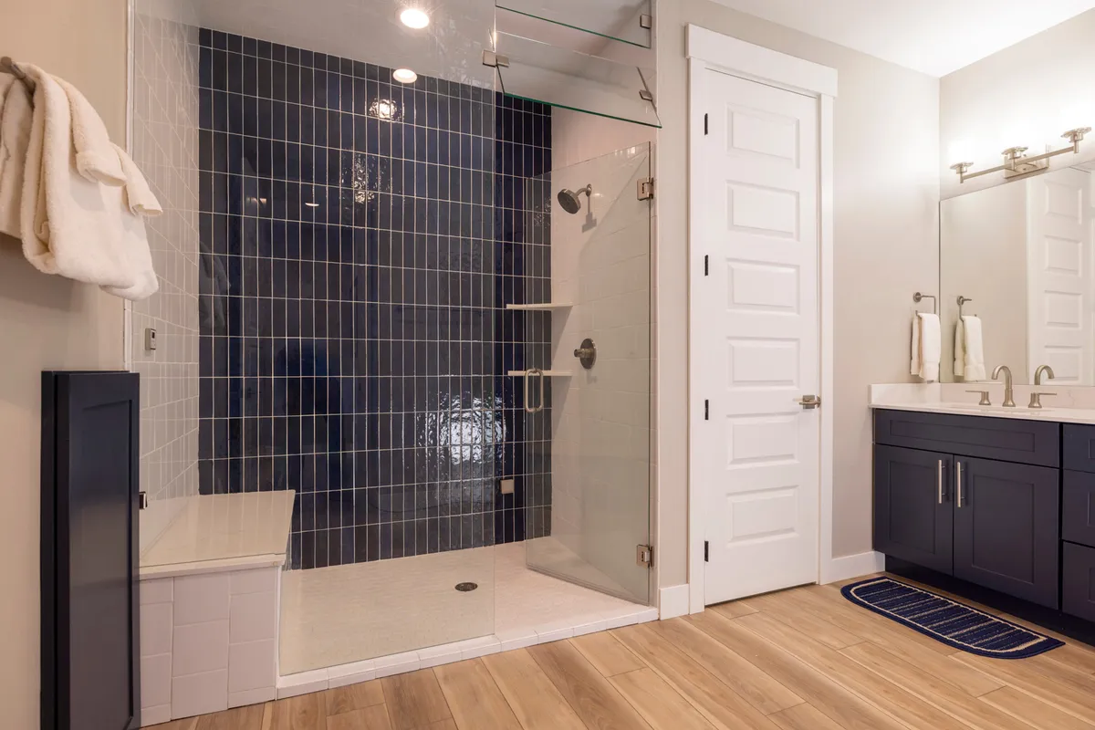 A modern, spa-inspired bathroom with a glass shower enclosure, blue tiled accent wall, and double vanity. The calm color palette and refined finishes create an atmosphere of relaxation and indulgence.