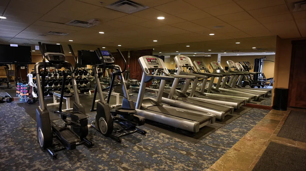A bright and energetic fitness room showcasing treadmills, elliptical machines, and a dumbbell rack. The space is designed for both individual and group workouts, allowing guests to stay active during their retreat.